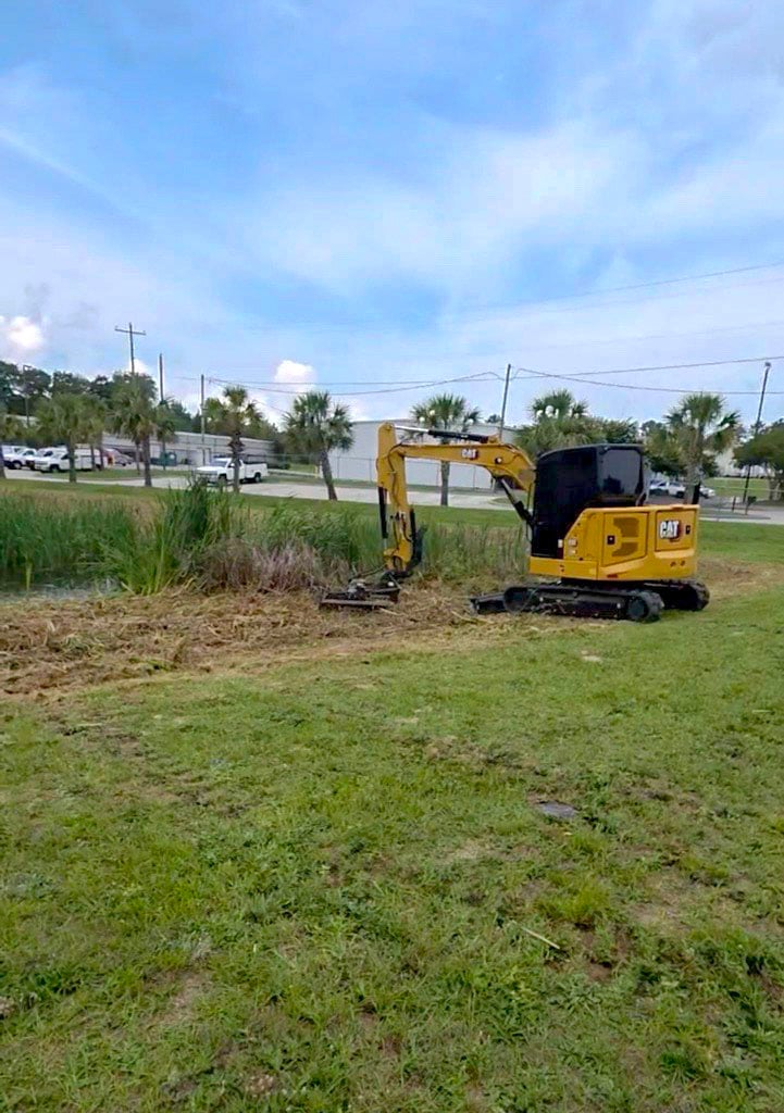 Compact excavator working along vegetation beside a pond