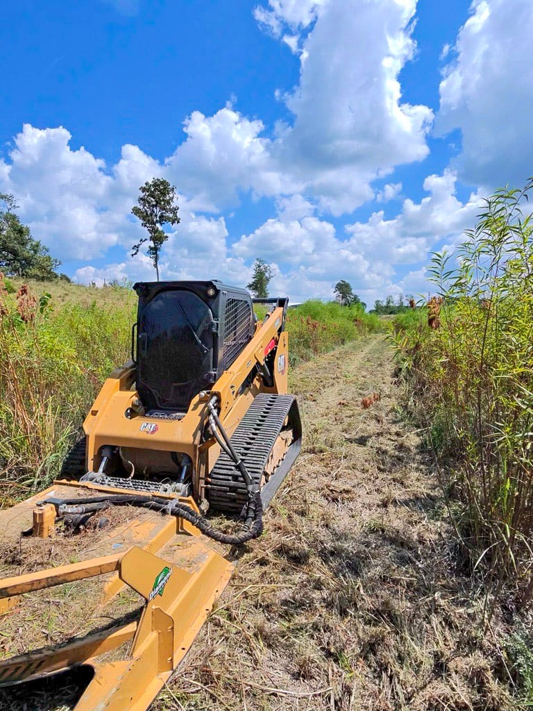 Tracked skid steer with a rotary brush cutter clearing tall field vegetation
