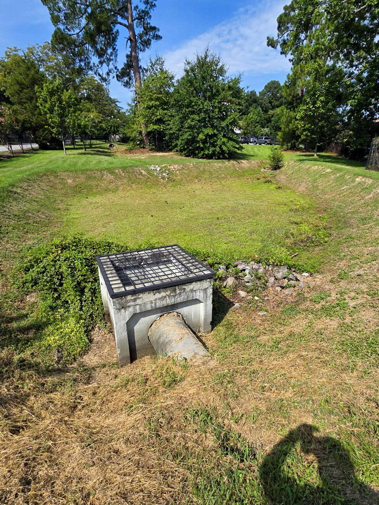 Metal debris screen covering a concrete stormwater outlet in a mowed basin