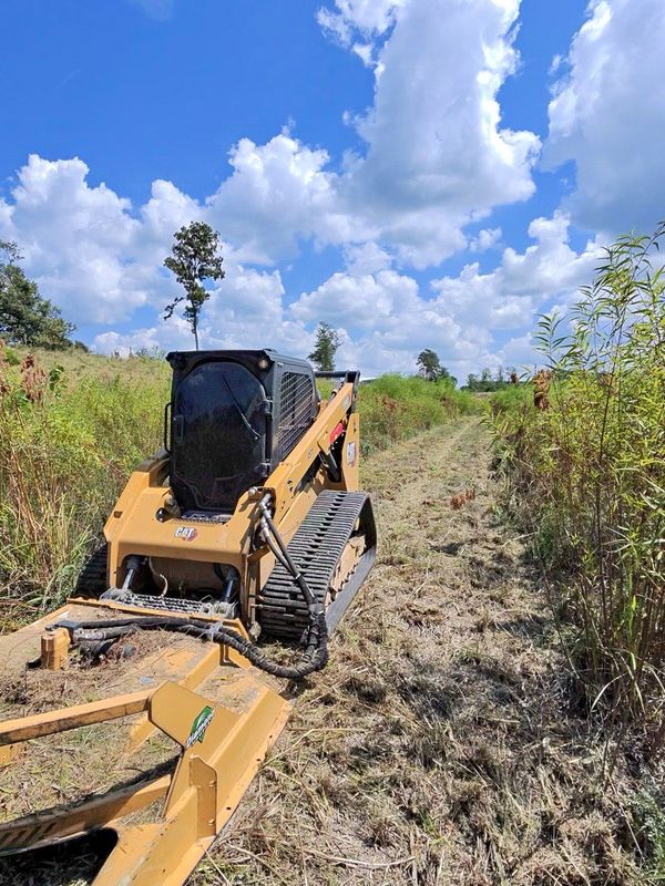 Tracked skid steer with a rotary brush cutter clearing tall field vegetation